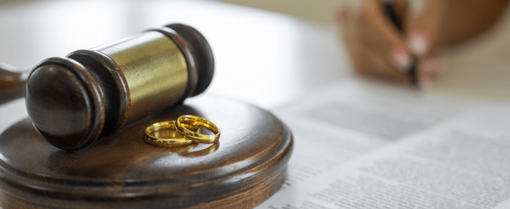 Gavel and wedding rings on document, person writing in background.