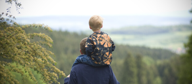 man with child on his shoulders, looking over a mountain