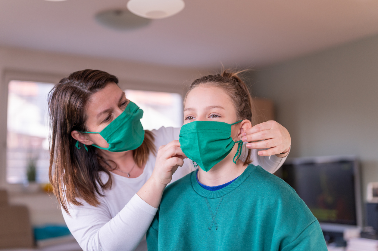 Mother putting on daughter's mask before she goes out.
