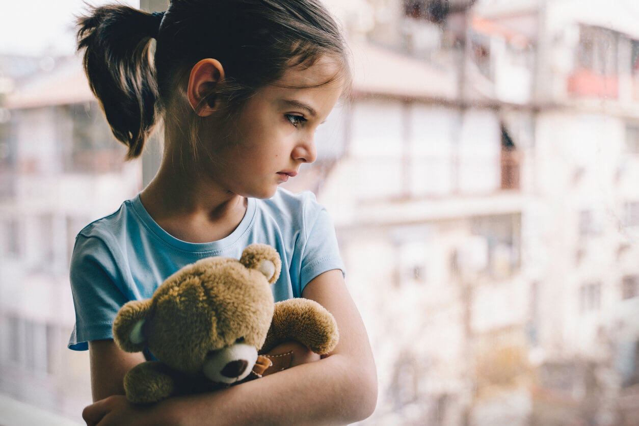 Little girl with sad expression hugging teddy bear.