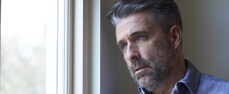 Visibly saddened middle-aged man looking out his window