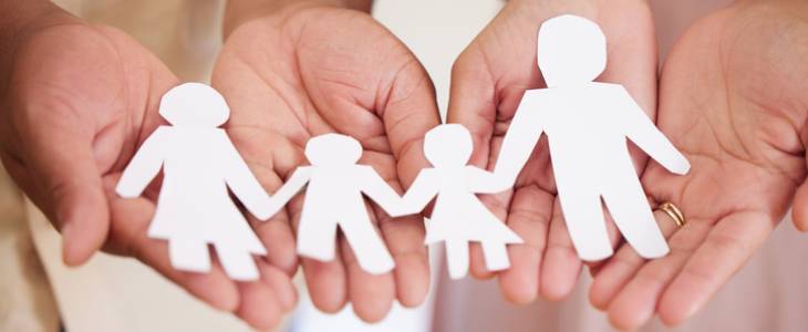 Hands holding a paper cutout of a family.