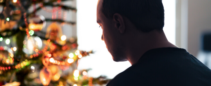 Sad man looking at Christmas tree.