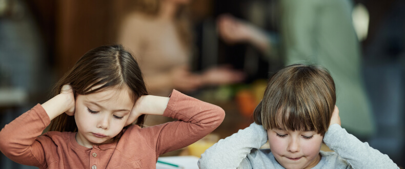 Children covering their ears while parents argue in background