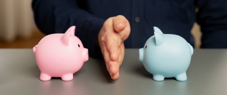 Hand dividing pink and blue piggy banks on a table.