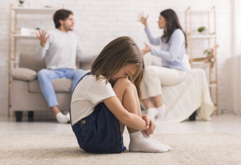 Little girl crying after parents quarrel at home, sitting alone with her head down, hiding her face in knees, selective focus